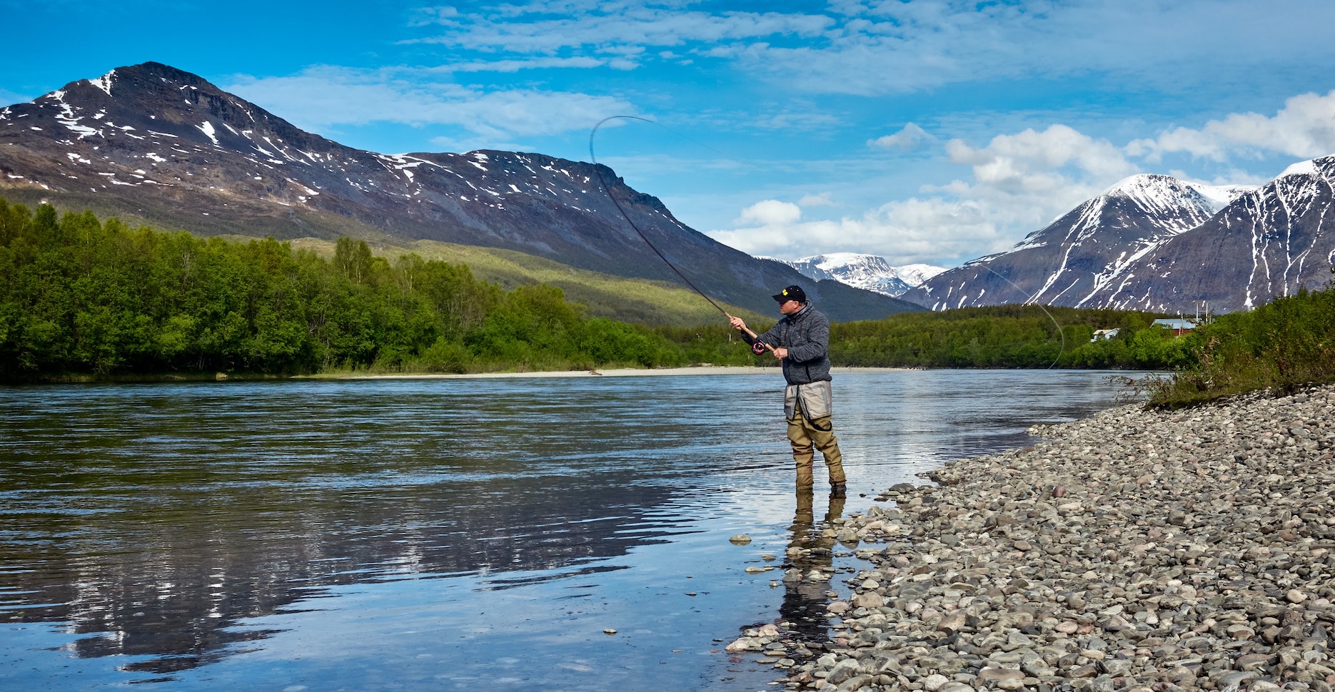 An image of a man fishing in a pond in front of the mountains